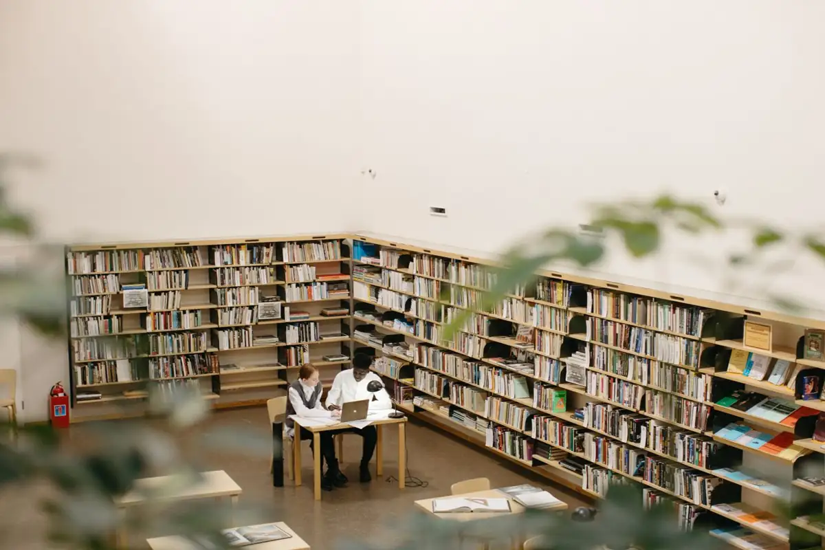 Two students studying together with a laptop and open books in a library.